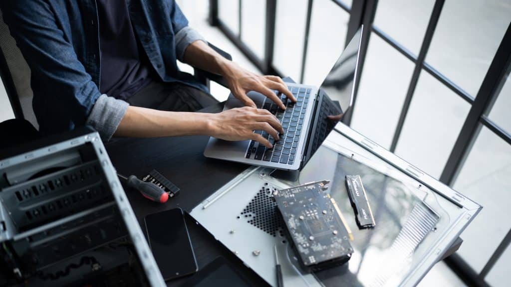 Business professional working on laptop next to open computer hardware components during IT hardware upgrade